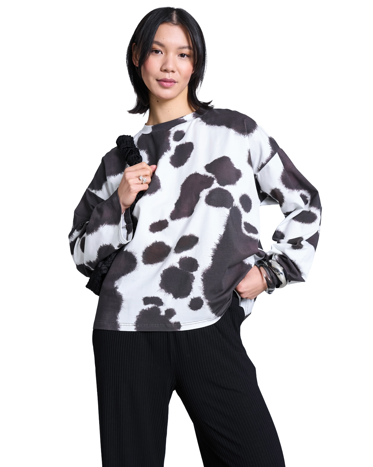 A person wearing a long-sleeved, white shirt with a black cow-print pattern and black trousers.
