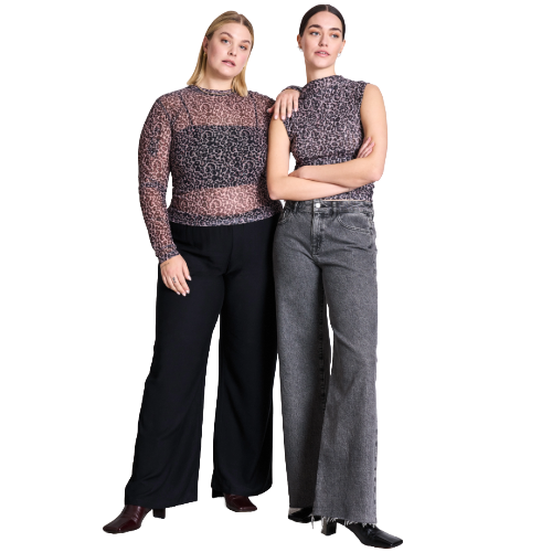 Two women stand side by side. One wears a long-sleeve patterned top with black pants, and the other wears a sleeveless patterned top with wide-leg gray jeans. Both look confidently at the camera.