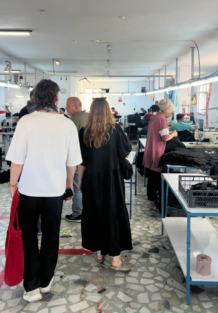 JAN 'N JUNE Team visitng a denim production where items are sewn and inspected by people in the background.