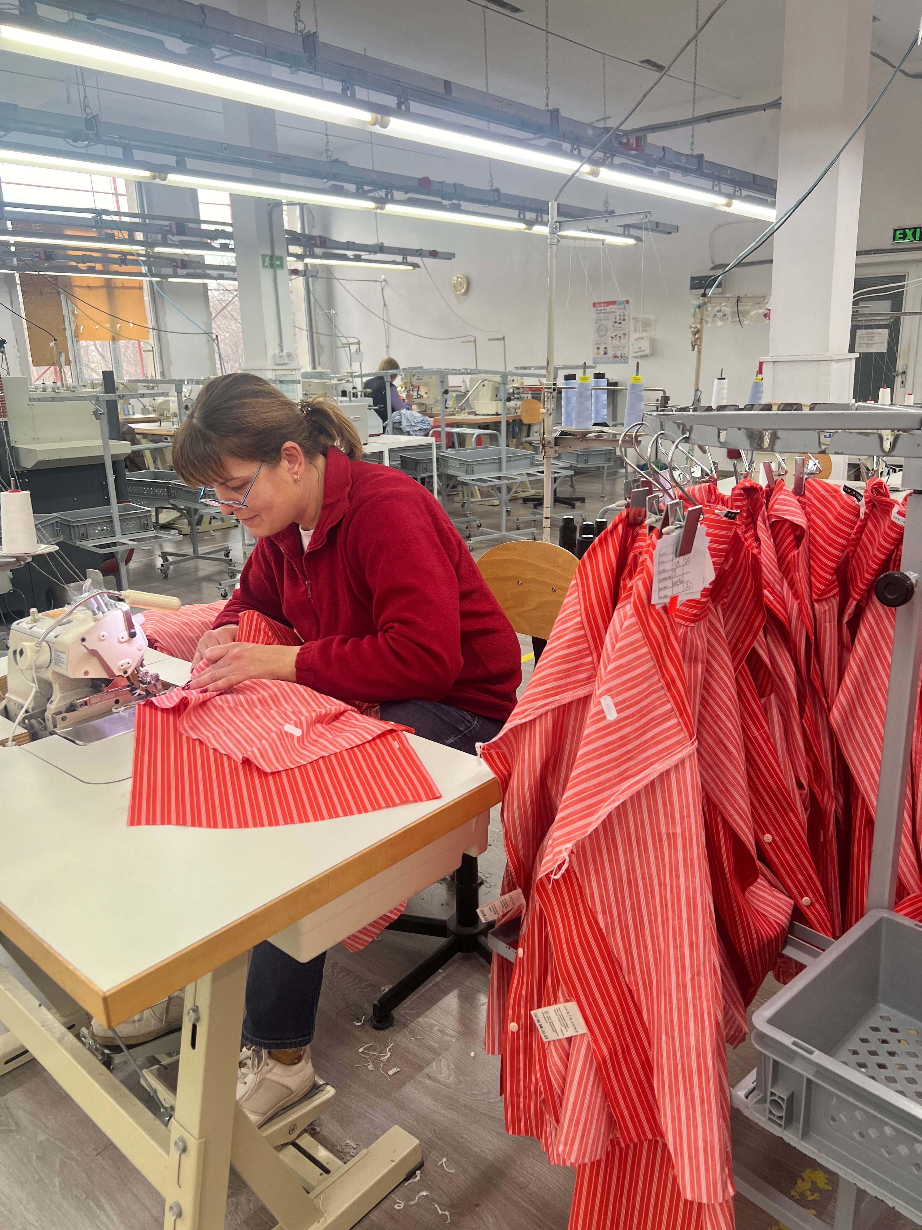 Woman with glasses sewing a red/white striped piece of clothes from a light woven fabric.